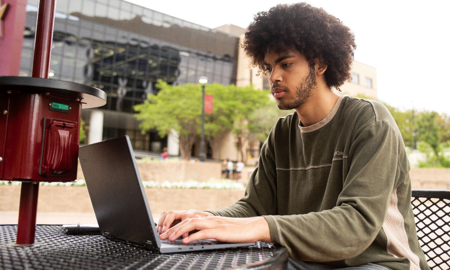 Student working on laptop with Alkek Library in background