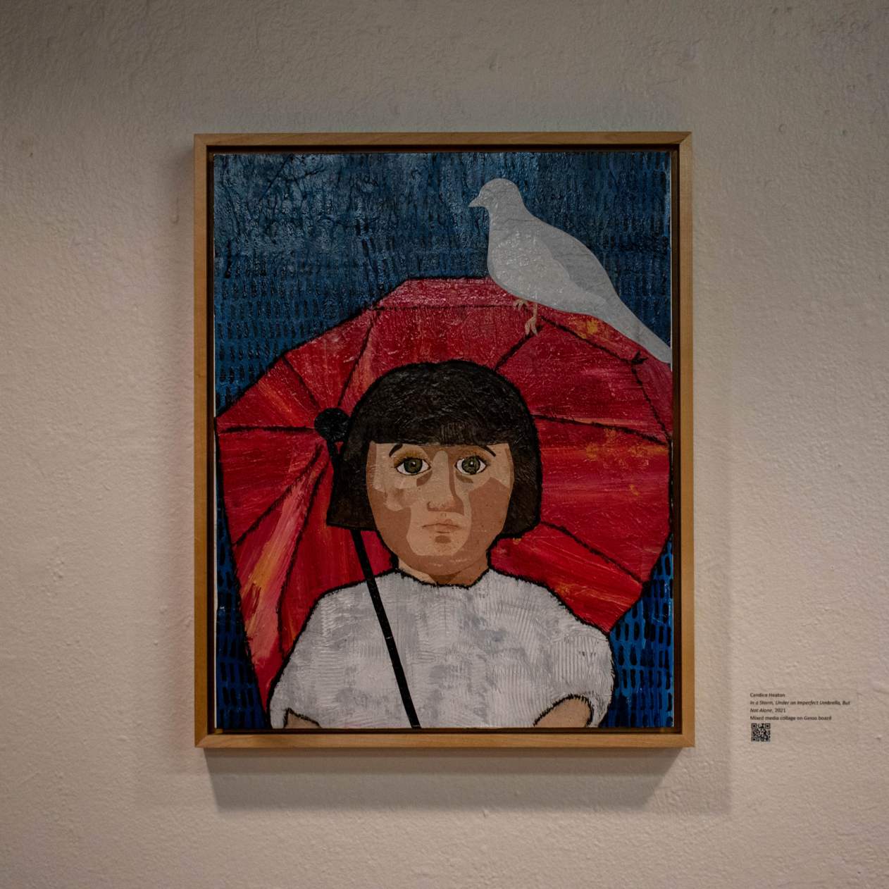 Gesso and mixed media textured painting of a person in white under a red umbrella with a white bird perching on it all on a blue background. Hung on a white wall.