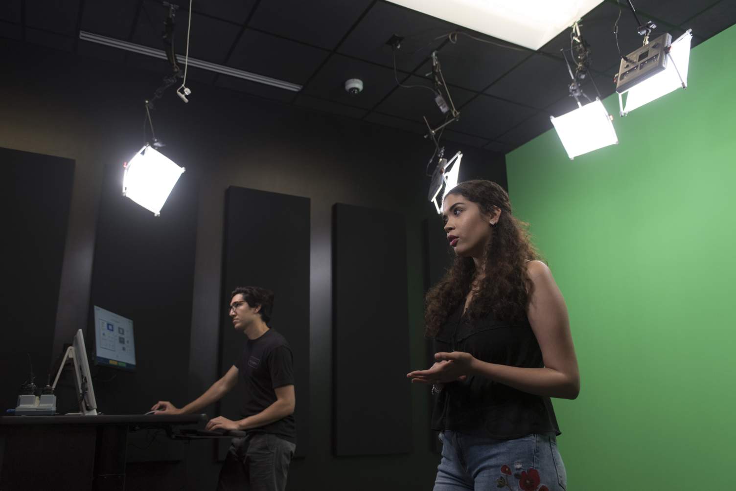 Woman in studio lighting and green screen background and man operating computer