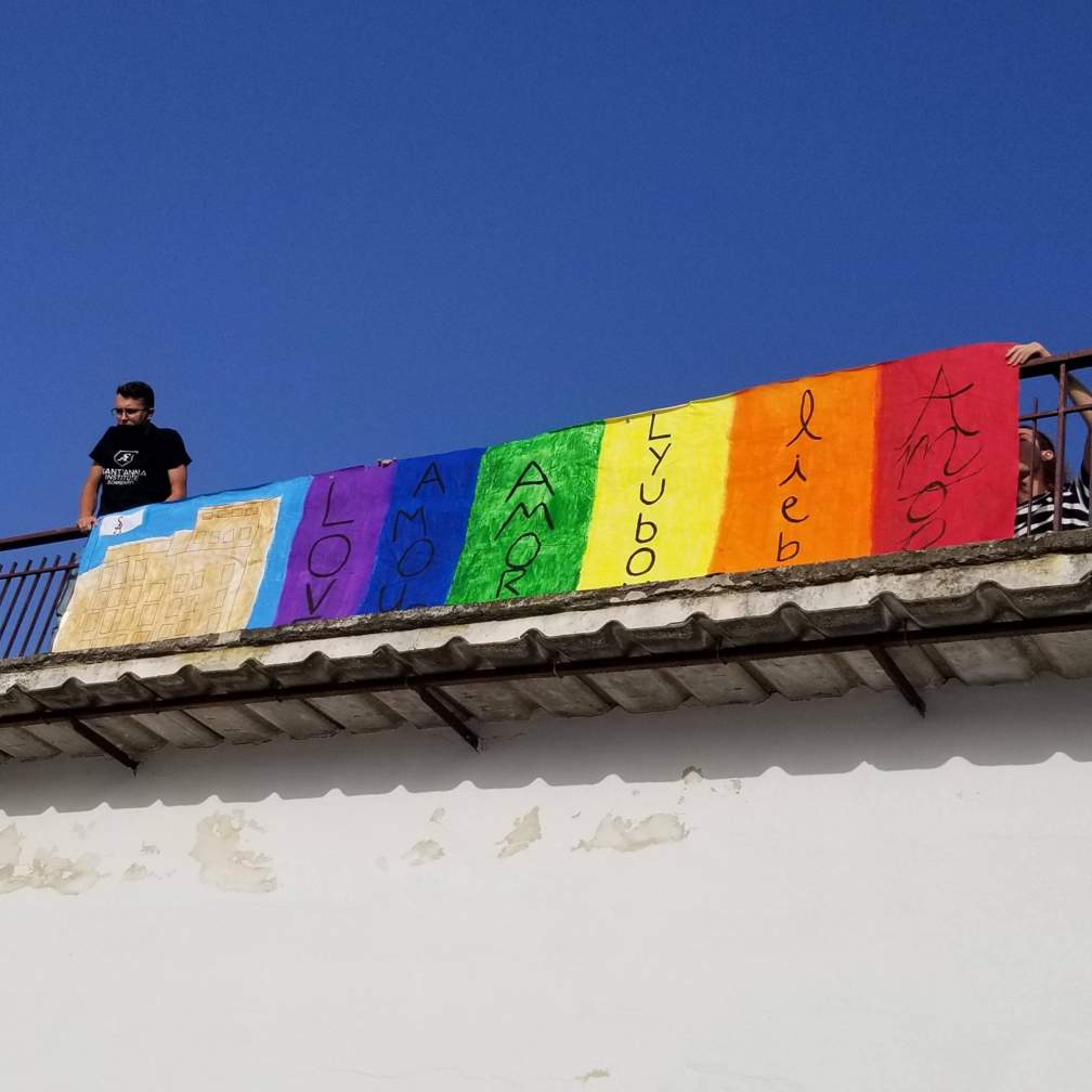 A large Pride banner with the word "love" in several different languages is hung from a railing